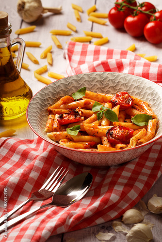 Penne pasta with tomato sauce and fresh basil in a bowl. Tablecloth background. Close up.