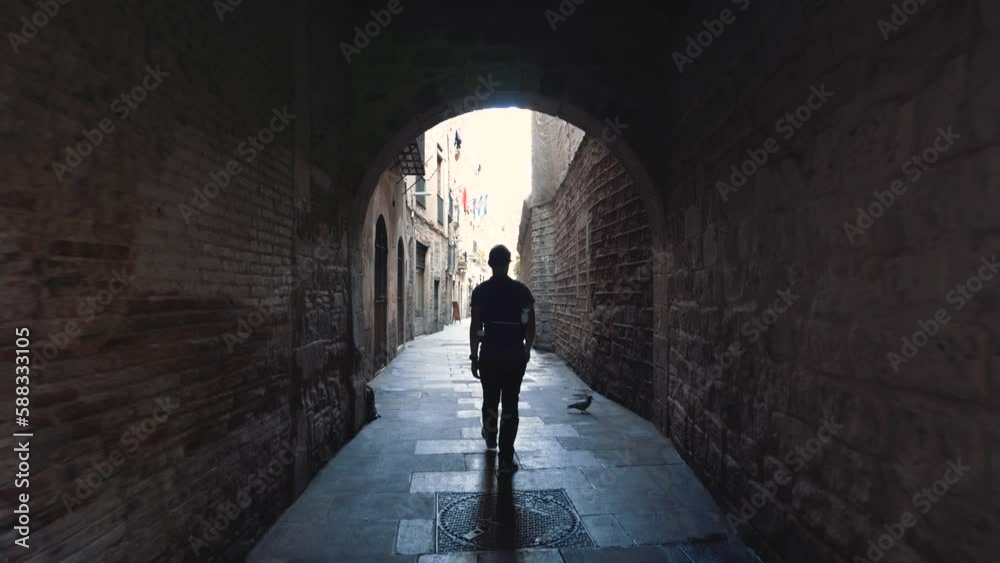 Gimbal shot of young man walking through medieval arch in Gothic Quarter streets of Barcelona, El Born, Catalonia, spain, on a warm summer day in narrow old town Spanish street; tourist walking Gimbal shot of young man walking through medieval arch in Gothic Quarter streets of Barcelona, El Born, Catalonia, spain, on a warm summer day in narrow old town Spanish street; tourist walking