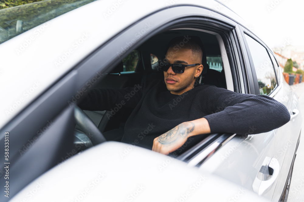 Serious young adult man seen through open driver's window. Focused guy in sunglasses driving his modern car. High quality photo