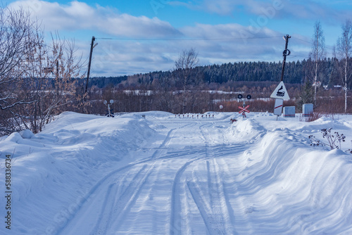 Countryside road crosses railroad track at winter day.