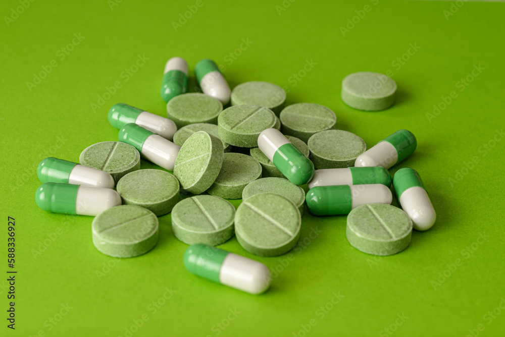 Scattered green and white capsules and pills on green background Scattered green and white capsules and pills on green background
