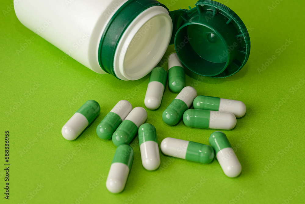 Green and white pills, opened white container and scattered green and white capsules