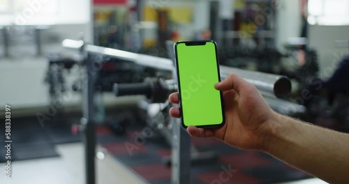 Wallpaper Mural Male hand holding smartphone in gym, fitness app for bodybuilding, green screen. Torontodigital.ca