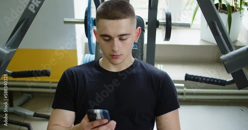 Portrait of guy in gym while resting between a workout uses phone body strength fit health male strong healthy muscular athlete guy physical young arm model mobile caucasian endurance close up. photo