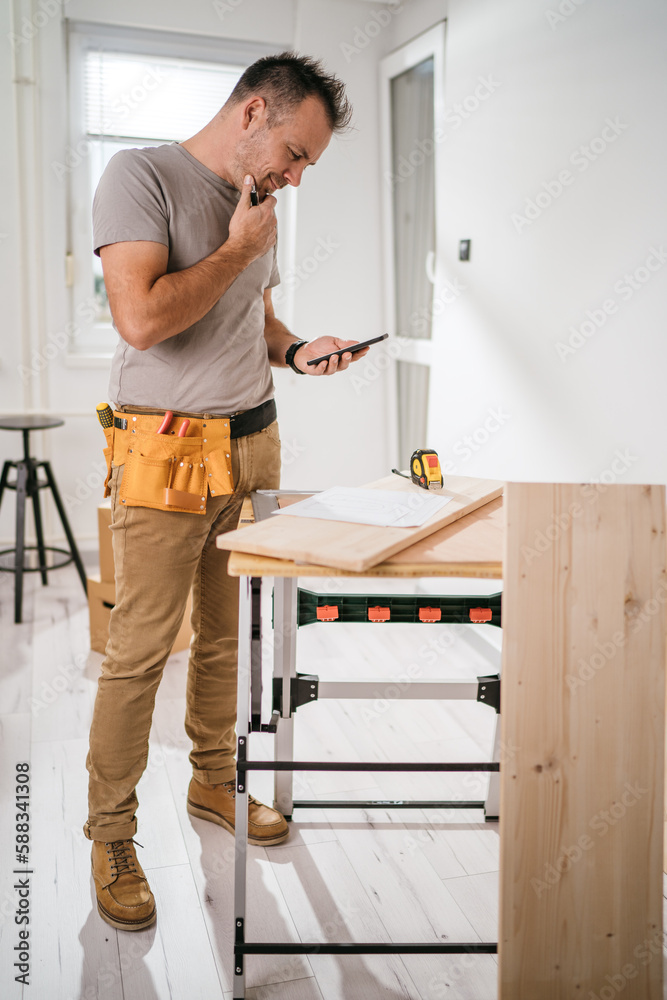 Hard working carpenter standing in front of his work desk , reading blueprint and thinking about the project