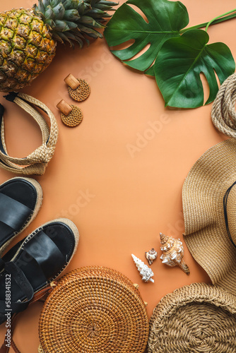 Colorful summer female fashion outfit flat lay. Straw hat, bamboo bag, wicker shoes, pineapple over beige background, top view, wide composition. Summer fashion, holiday concept