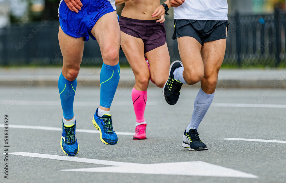three runners male and female athletes run marathon race, jogger legs in compression socks run city road