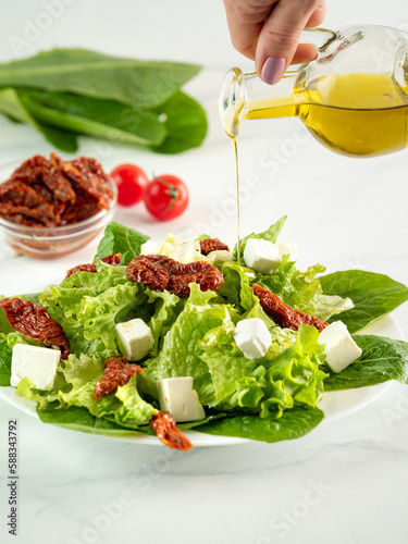 Salad of sun-dried tomatoes  cheese and salad leaves. Olive oil pouring on salad