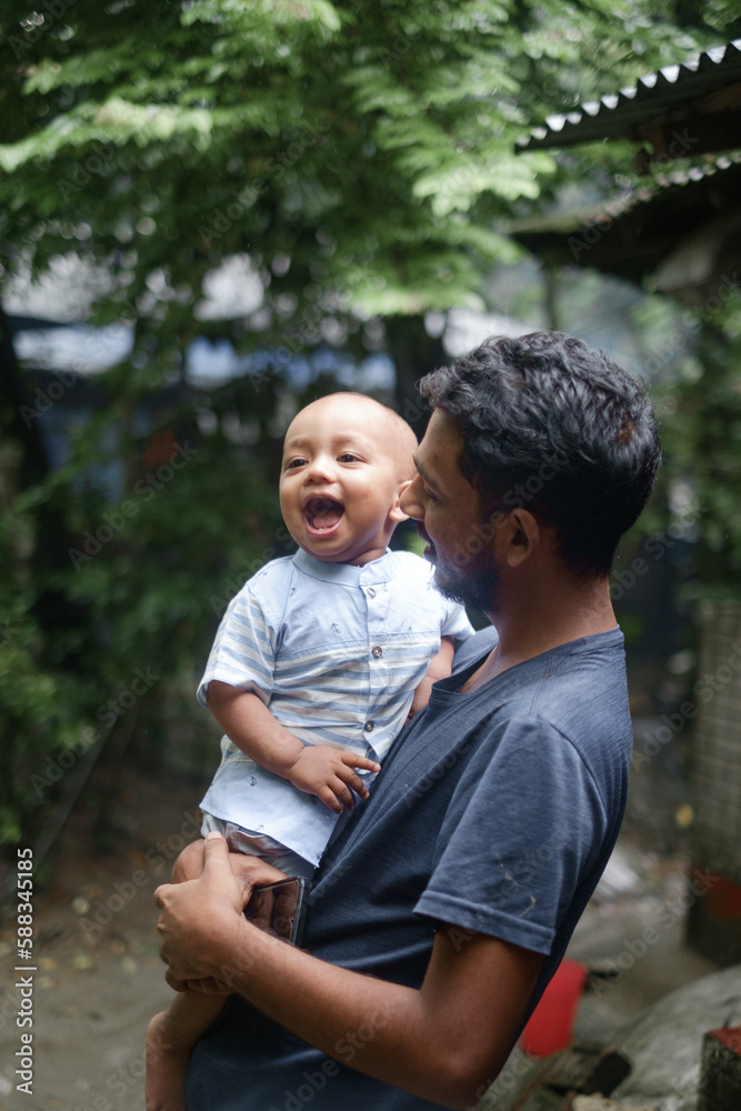 Fototapeta premium South asian young rural father holding his little son, village baby boy playing with his young dad, lovely family moments in outdoor 