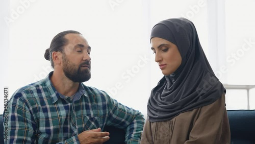 Muslim couple talking at home, obedient wife in hijab nodding head, relationship