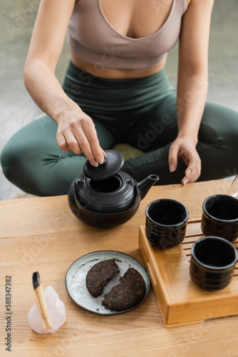 cropped view of woman in sportswear brewing puer tea in Chinese teapot.