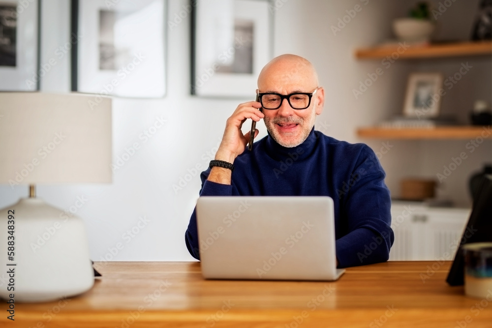 Middle aged businessman using smartphone and laptop while working from home Middle aged businessman using smartphone and laptop while working from home