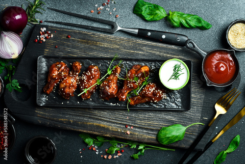 Fried buffalo chicken wings with honey sauce and sesame seeds on a black stone plate. On a dark background, close-up.
