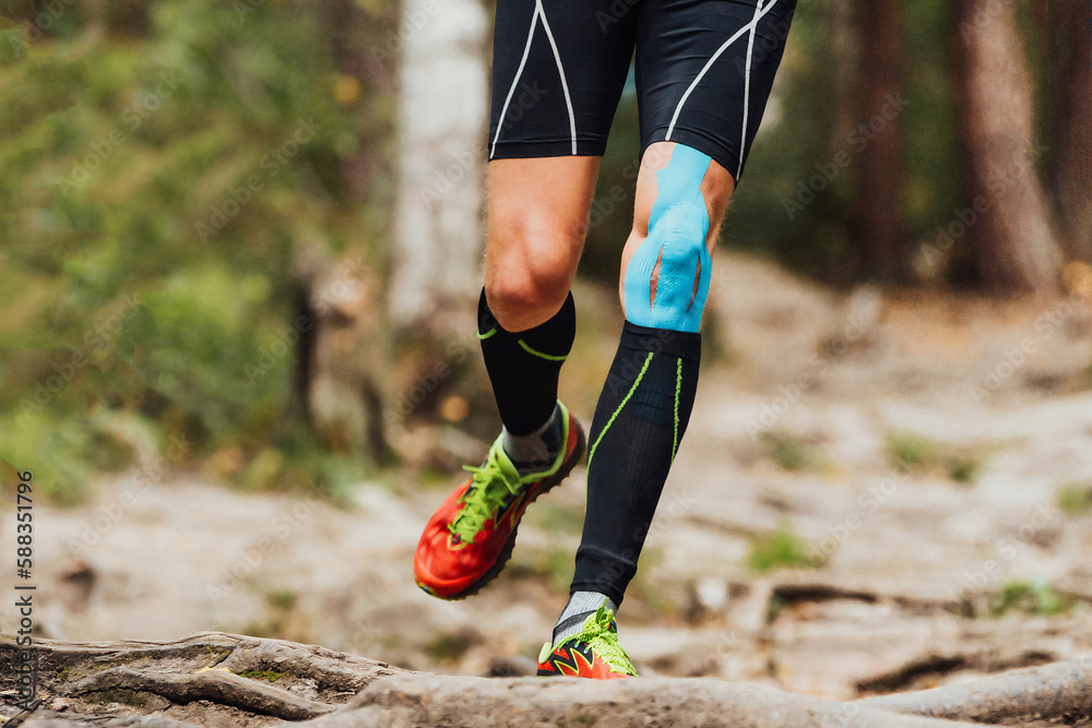 legs male runner with kinesio tape on knee running forest trail marathon,  black compression socks and blue kinesiotaping Stock Photo