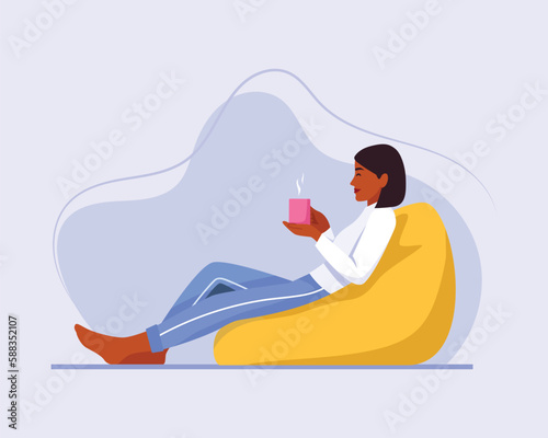 a dark-skinned girl with short hair sits on a chair (bag chair) with a cup of coffee or tea