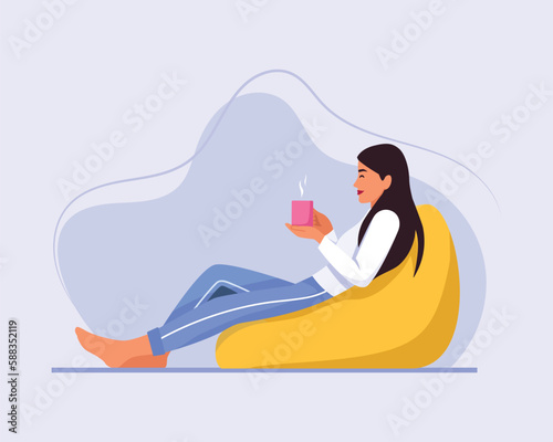 a fair-skinned girl with long hair sits on a chair (bean bag chair) with a cup of coffee or tea