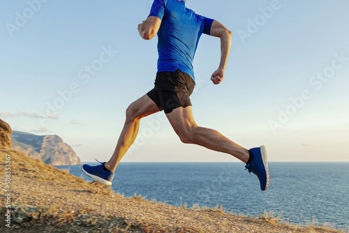 male runner run uphill  sea trail on withered grass  cross-country running race  blue shirt and black shorts