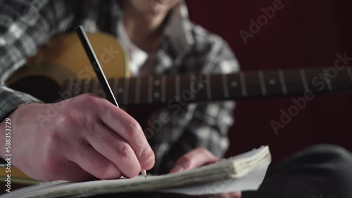 young man writing song lyrics with acoustic guitar in cozy room.