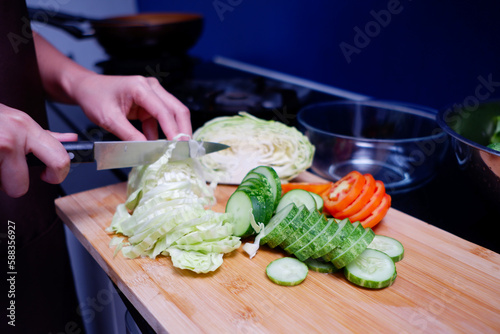 Young female hand using a knife to cut fresh vegetables on a cutting board.