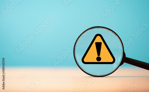 Yellow triangle caution warning sign inside of magnifier glass on blue background and copy space for maintenance notification error and risk concept. photo