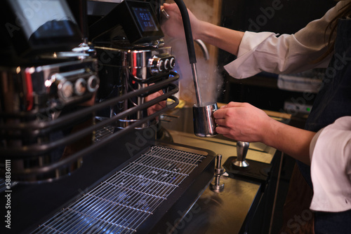 Close up of a barista heating milk for coffee in a cafe on a coffee machine.