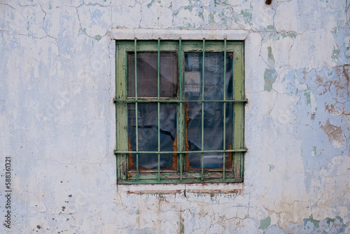 The window of a poor man's house with a grille on a peeled wall painted white with lime