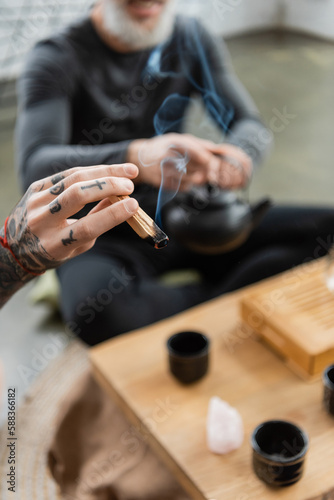 cropped view of tattooed man holding wooden palo santo stick in yoga studio.