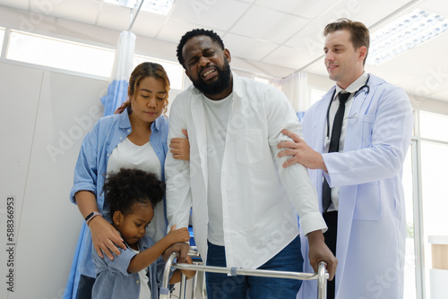 Doctors examine a black patient who has had an accident with a broken leg accompanied by his wife and child.