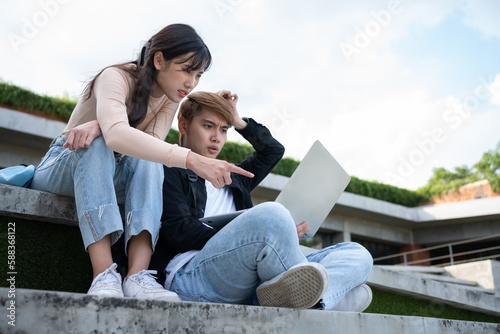 Asian students sitting on steps and use computer laptops to discuss before exams, Student lifestyle at university. Group of student do a project together © Prot