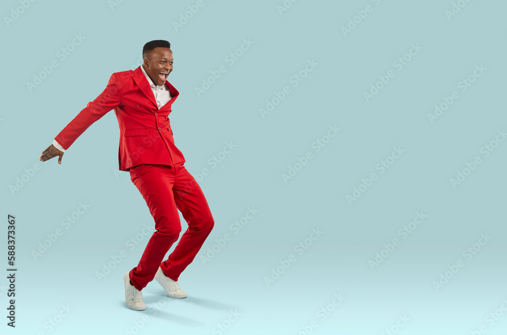 Happy African man in red suit having fun in fashion studio. Attractive ethnic guy in cool modern trendy outfit feeling elated and overjoyed dancing and jumping on light blue text copyspace background Happy African man in red suit having fun in fashion studio. Attractive ethnic guy in cool modern trendy outfit feeling elated and overjoyed dancing and jumping on light blue text copyspace background