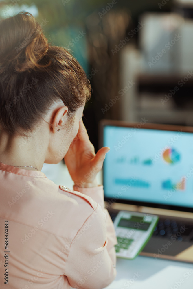 Seen from behind modern woman with calculator and laptop
