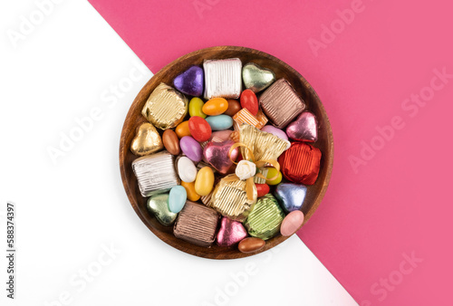 Chocolate candies, top view plate of chocolate candies. Wrapped multicolored foil. Almond candies. Isolated white and pink background. Copy space. Traditional Turkish feast called bayram sweets. photo