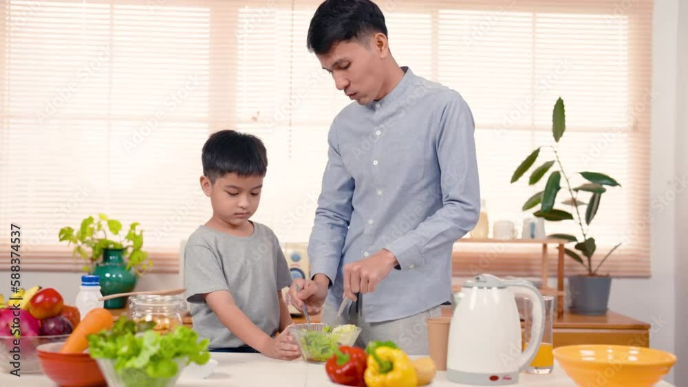 4K, Father standing with son making vegetable salad, picking it up taste, using spoon carve green vegetables feed it son standing next, son raised hand cover mouth because doesn't like eat vegetables. 4K, Father standing with son making vegetable salad, picking it up taste, using spoon carve green vegetables feed it son standing next, son raised hand cover mouth because doesn't like eat vegetables.