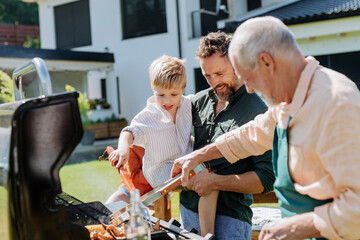Multi generation family grilling outside on backyard in summer during garden party