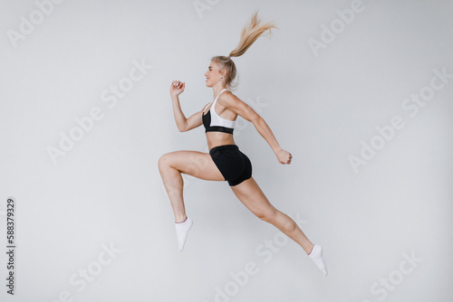 Beautiful fitness woman in a jump in sportswear on a gray background, dynamic movement.