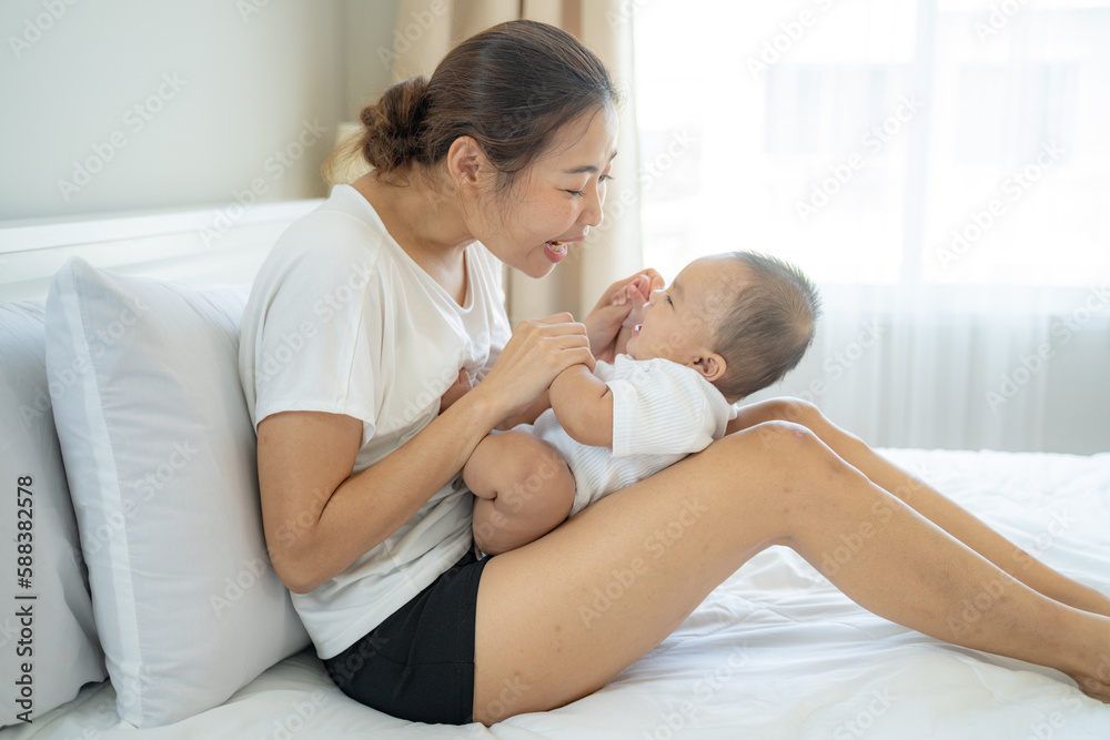 young Asian mother is playing with her newborn baby on the white bed in a home in a morning.Concept of mom day,newborn,baby,parenthood,mother day,childhood,New life,maternity,love,new family member young Asian mother is playing with her newborn baby on the white bed in a home in a morning.Concept of mom day,newborn,baby,parenthood,mother day,childhood,New life,maternity,love,new family member