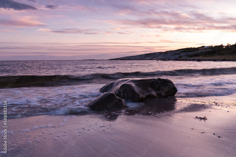 Naklejka premium Sea coast, waves crashing against a stone in the water, sunset