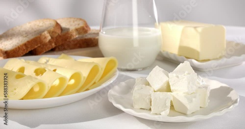 dairy products on a light background. milk cheese bread and butter on a white tablecloth close-up. slices of gouda cheese. piece of butter and a glass of milk with slices of bread in the background.