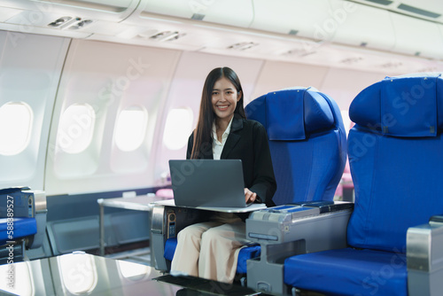 Asian business woman passenger sitting on business class plane while working on laptop computer with simulated space using on board wireless connection