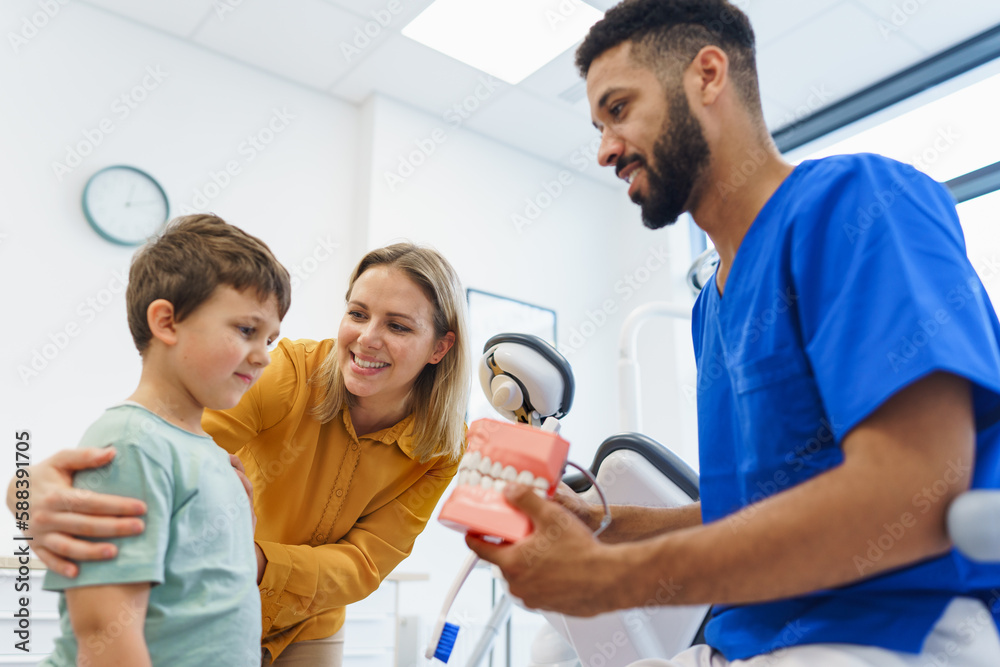 Young multiracial dentist showing little boy how to clean teeth, concept of children oral hygiene,prevention and dental health. Young multiracial dentist showing little boy how to clean teeth, concept of children oral hygiene,prevention and dental health.