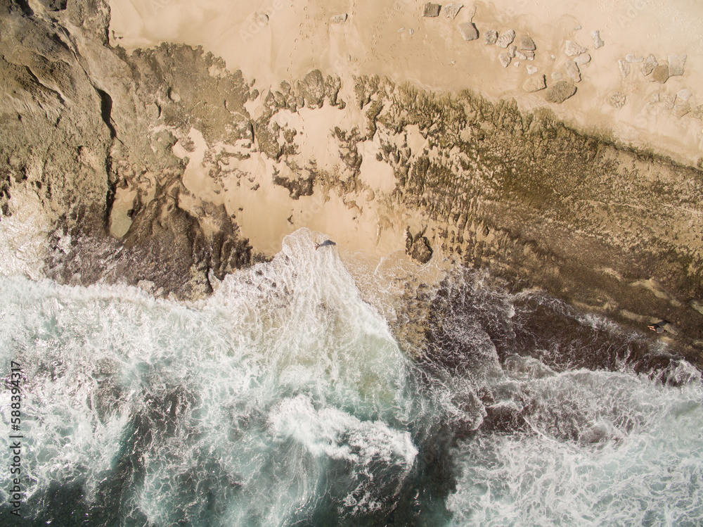 Sand and rock are being eroded away with each wave that crashes onto ...