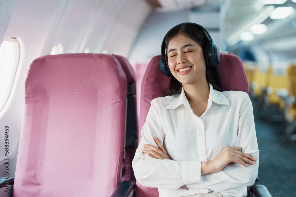 Young Asian attractive business woman passenger sitting on business class luxury plane while wearing wireless headphone for relax and working with tablet during the flight Young Asian attractive business woman passenger sitting on business class luxury plane while wearing wireless headphone for relax and working with tablet during the flight