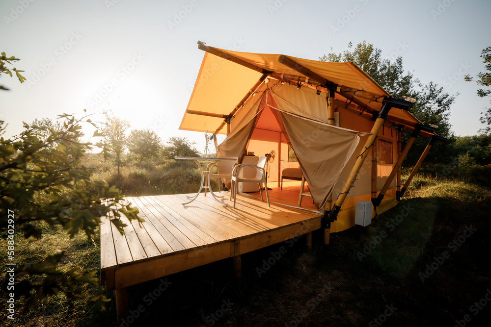 Cozy open glamping tent with light inside during sunset. Luxury camping tent for outdoor summer holiday and vacation. Lifestyle concept