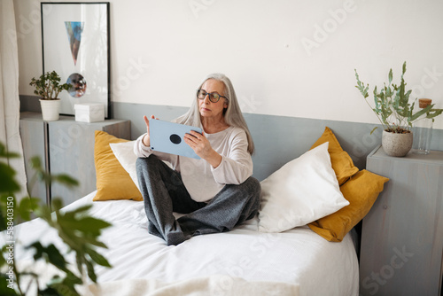 Senior woman sitting on bed with a digital tablet. photo