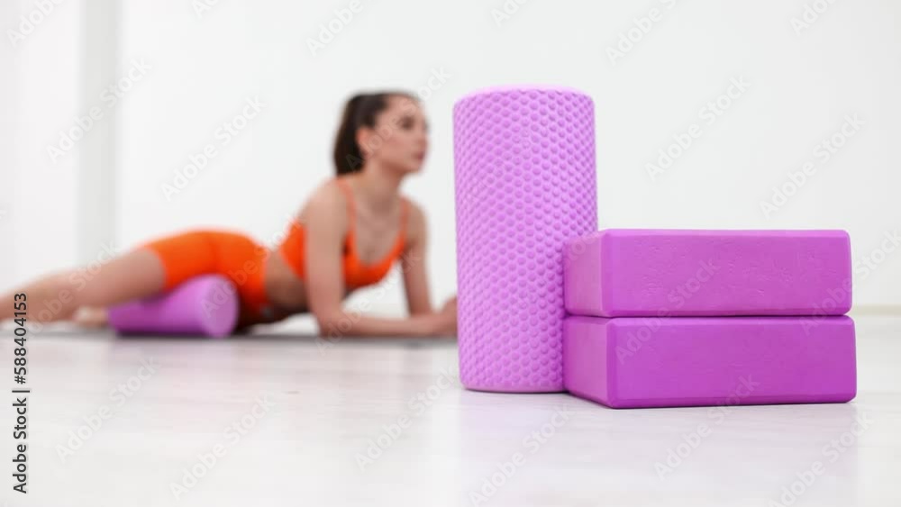 Fitness woman in sportswear is doing fitness with a foam roller. Work out on a yoga mat with a roller at home or at the gym. Active girl is engaged in fitness in the gym. MFR