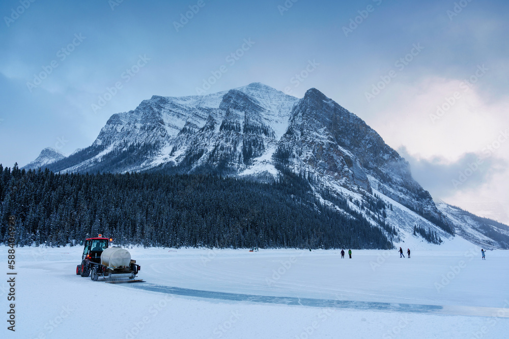 Tractor plowing snow on frozen lake preparing for natural ice rink in Lake Louise in the morning at Banff national park