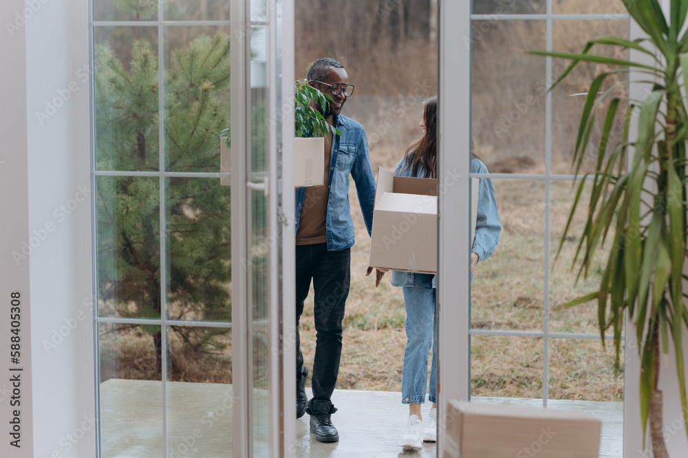 A young couple moves into a new house. an African-American man and his wife carry boxes into a new house.