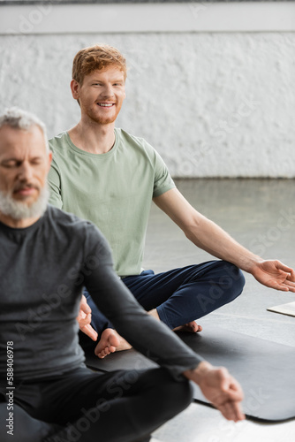 Cheerful redhead man doing gyan mudra and looking at camera in yoga studio.