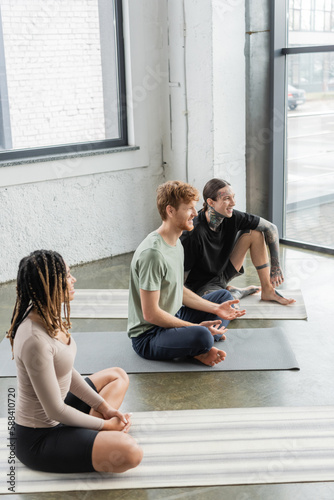 Young smiling multiethnic people talking on mats in yoga class.