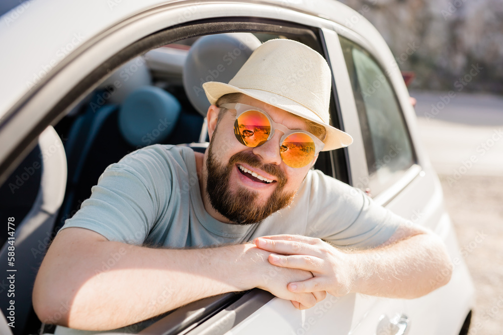 Naklejka premium Happy man sitting in white convertible car with beautiful view and having fun - travel summer vacation and rental car concept